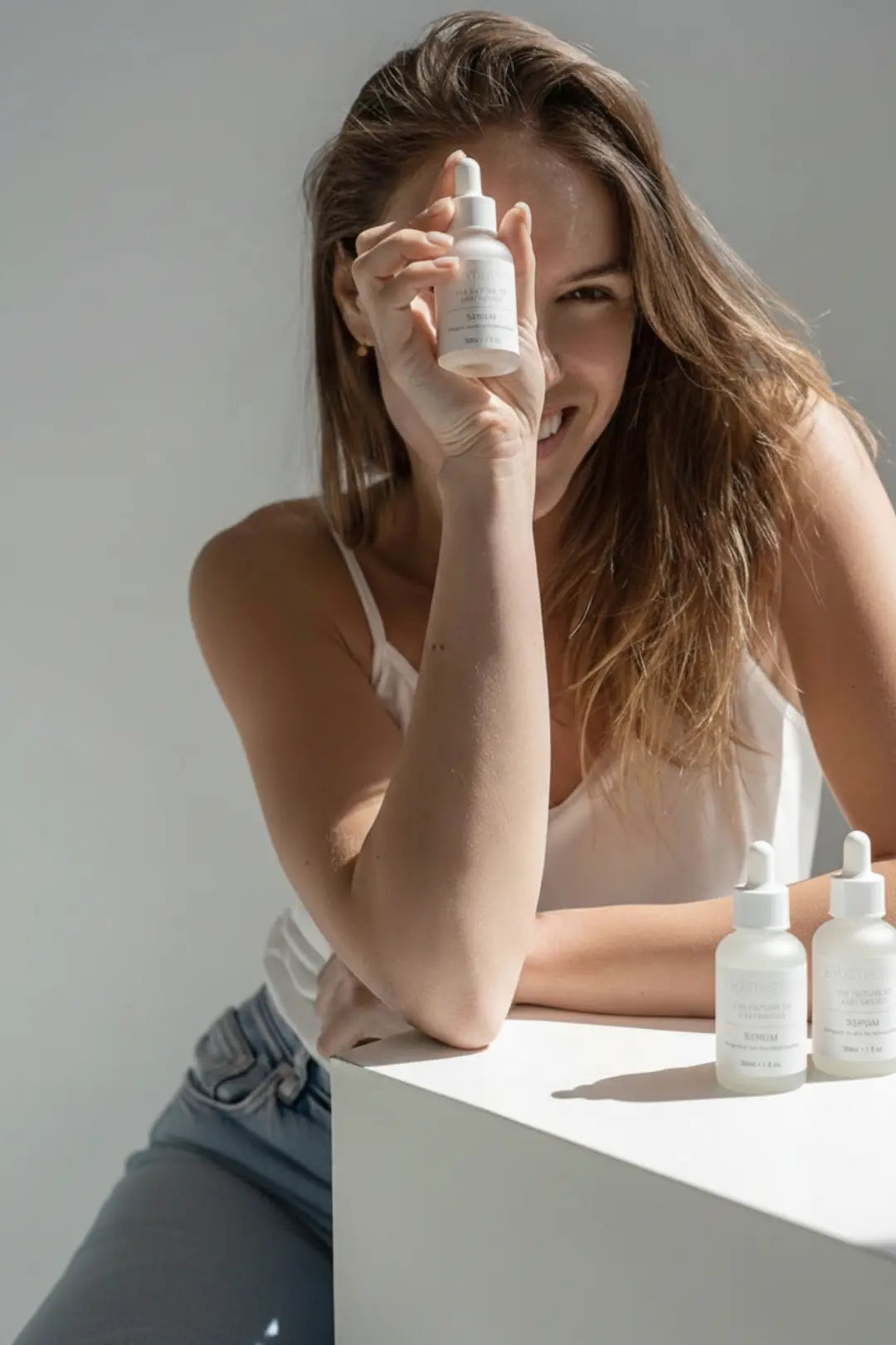 Woman holding a skincare bottle with more bottles on a surface in the background of exosthetics exosome serum bottles on their contact page